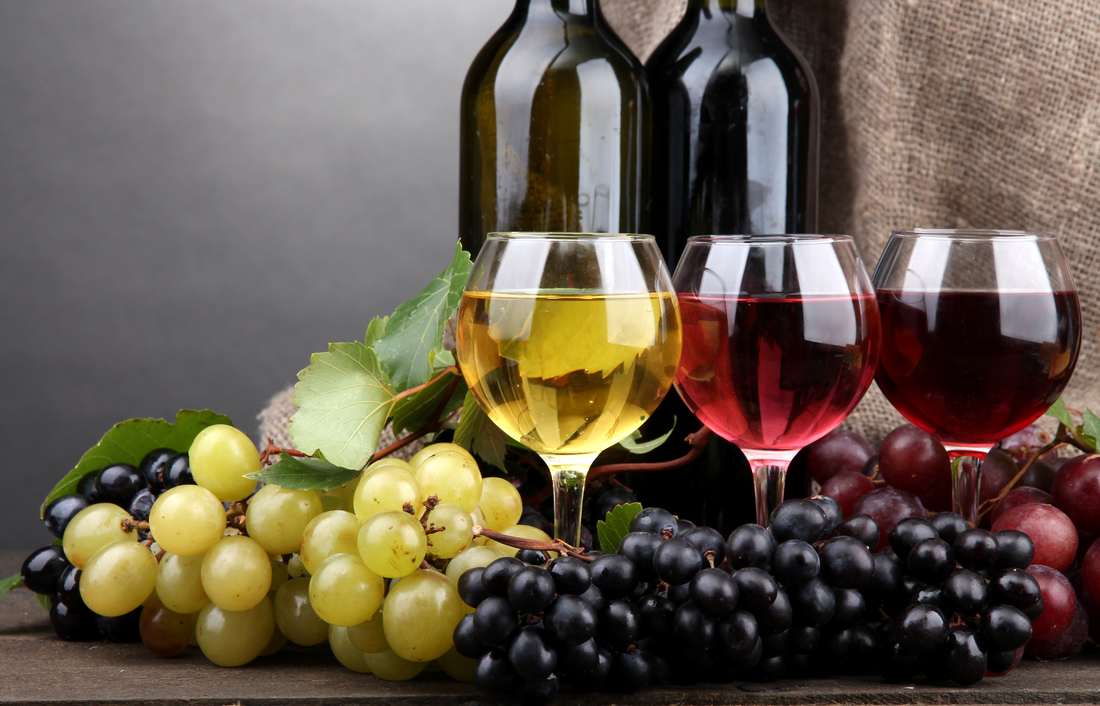 Bottles and glasses of red wine and red and green grapes on black background